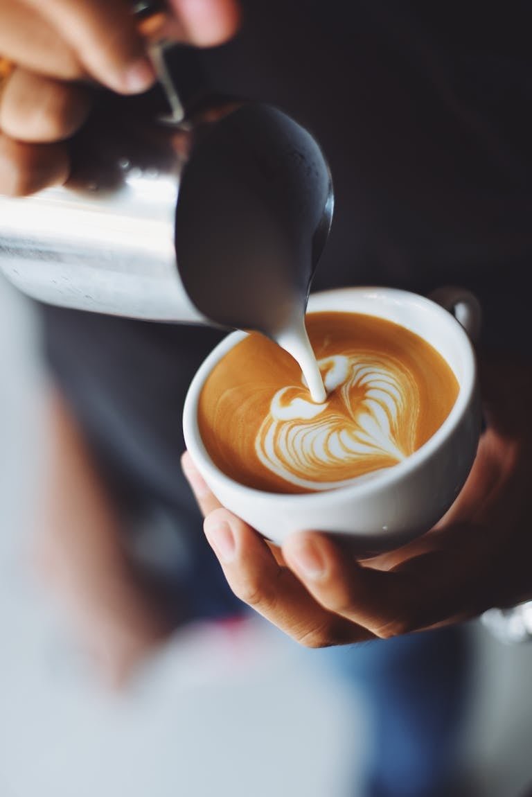 Close-up of barista pouring milk to create stunning latte art in a coffee shop setting.